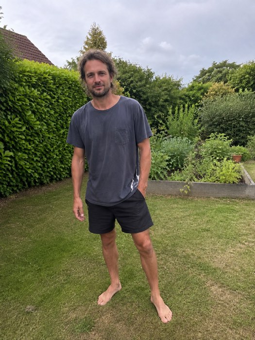 Philipp steht barfuß im Garten, bewölkter Himmel