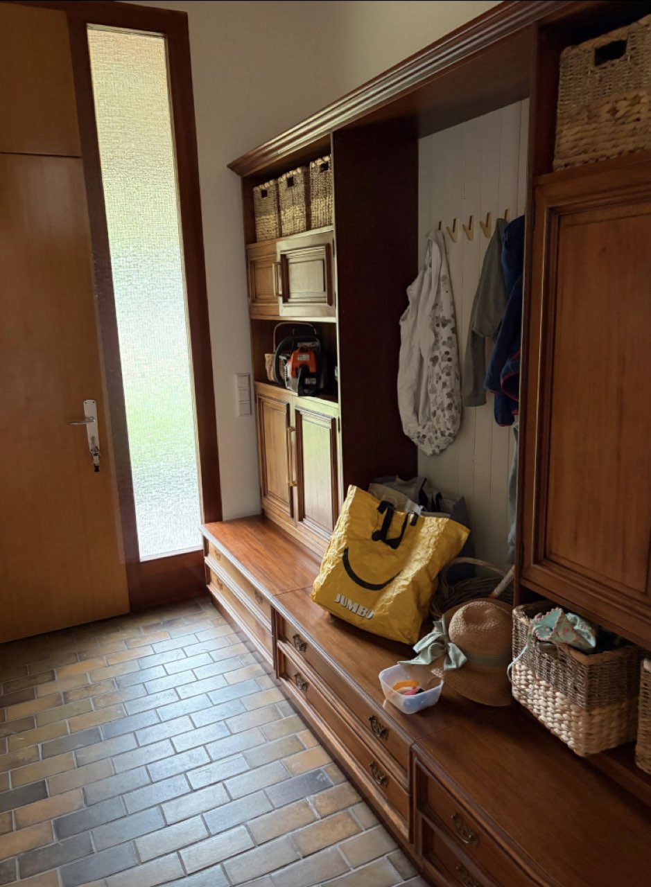 Der Eingangsbereich vorher: Massivholz-Garderobe mit vollen Haken, gelber Tasche, Hüten und einer Kettensäge im Regal