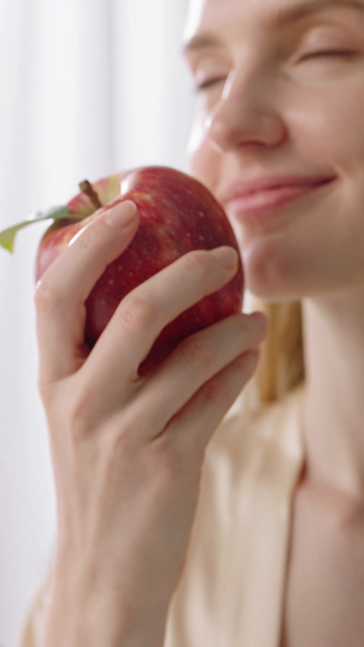 Frau hält den Apfel lächelnd ans Gesicht, weiches Werbelicht